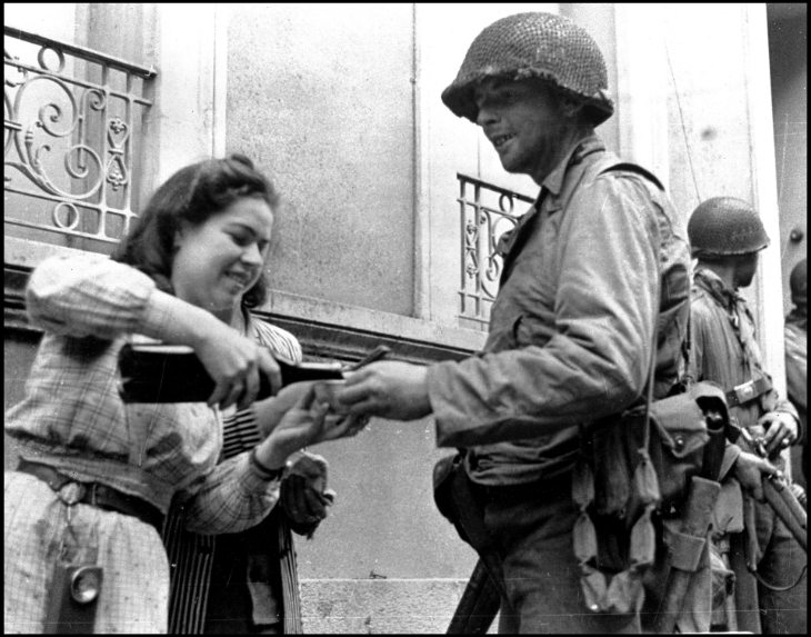 A young resident of Cherbourg (Manche) serves a glass of wine for an American soldier after the surrender of German troops during the Second World War. Photograph of June 27, 1944. | © Usis-Ditite / Leemage / Bridgeman Images via AFP