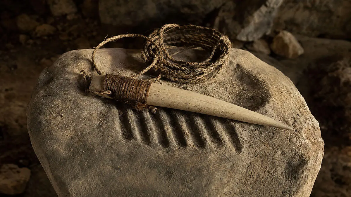 Contextual closeup on workbench: mammoth ivory tool with helical grooves on fabric and vege fibers